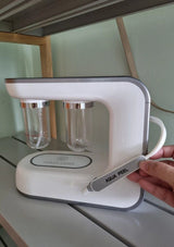 White electronic device with two clear containers on a light green wall background