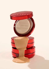 Red cosmetic compact with open lid showing cream inside on a beige background