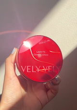 Hand holding a red compact with 'VELVET' branding against a neutral background