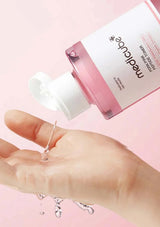 Hand holding a dropper with clear liquid next to a pink bottle labeled 'medicube' on a pink background