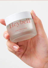 Hand holding a jar of Heybell cream against a white background