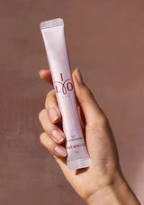Hand holding a pink skincare product tube with 'I LOO' branding against a brown background