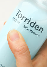 Torriden Skin Booster bottle held by a hand with a blurred background