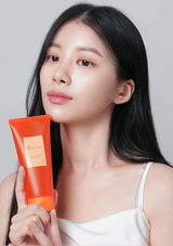 Woman holding an orange skincare product against a plain background