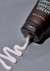 Shaving cream being squeezed from a tube labeled 'Comfort Shaving Cream' on a gray background