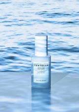 Skincare serum bottle with blue label on a reflective water surface