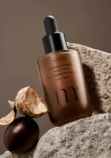 Skincare serum bottle with a natural shell and leaf on a stone surface