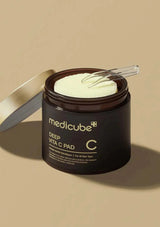 Medicube Deep Vita C Pad jar with a spoon on a beige background