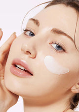Woman applying cream under her eyes with a white background