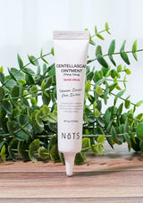 Tube of NOTS Centella Scar Ointment on a wooden surface with green leaves in the background