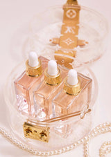Set of three clear dropper bottles with gold caps on a decorative stand with pearls.