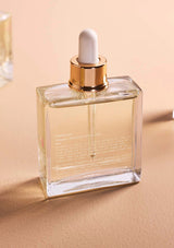 Clear glass bottle with gold cap and white dropper on a beige background