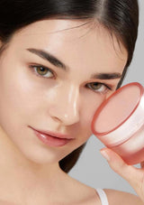 Woman holding a pink cosmetic container against a neutral background