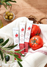 Three tubes of olive oil on a wooden surface with tomatoes and olives.