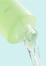 Green bottle with clear liquid being poured against a light blue background