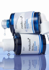 Two bottles of Medicube skincare product on a reflective surface with a white background