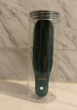 Black hairbrush with green handle in a clear plastic stand against a marble wall.