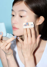 Woman applying makeup with a brush and compact powder on a light blue background