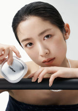 Woman holding a compact mirror with a brand logo, wearing a pearl necklace.
