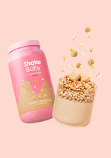 Pink 'Shake Baby' protein shake container with a glass filled with powder and toppings on a pink background