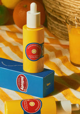 Yellow dropper bottle with a red label on a blue box against an orange and yellow striped background.