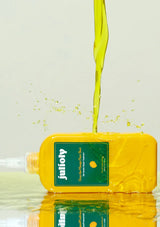 Yellow bottle of Juifoly with green label being filled with yellow liquid on a light gray background