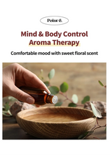 Hand holding a bottle of essential oil over a wooden bowl with a blurred background of greenery.