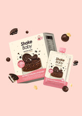 Shake Baby protein powder packaging shown on a soft pink background, including a carton and a single pouch with chocolate cookie graphics and floating cookie pieces.