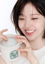 Person holding a white cup with a green logo, smiling.