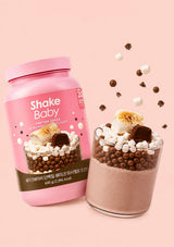 A pink container of Shake Baby Protein Shake in Marshmallow Chocolate flavor, shown against a solid pale pink background.