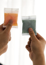 Two hands holding packets of different colored powders against a white background