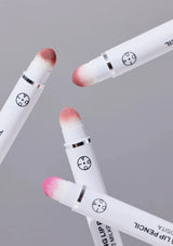 Three white lip pencils with pink and red tips on a gray background