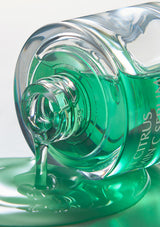 Close-up of a green bottle with liquid spilling out on a light gray background