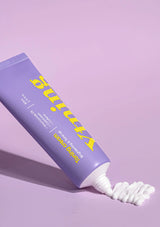 Purple tube of toothpaste with white bristle brush on a light purple background