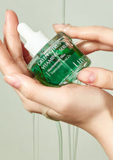Hand holding a green skincare serum bottle labeled 'Green Citrus Vitamin C Serum' with a neutral background.