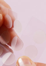Close-up of clear adhesive patches on a finger against a light pink background