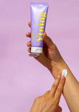 Hand holding a tube of 'Yuning' skincare product against a pink background