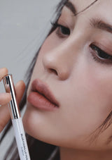 Close-up of a person holding a cosmetic pencil near their face against a neutral background