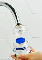A hand holding a clear bottle with a blue cap and a visible PURESOME label, positioned under a chrome faucet with a clear filter attachment partially unscrewed.