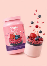 A pink container of Shake Baby protein shake powder with a berry yogurt flavor, shown against a solid pale pink background.