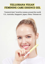 A smiling blonde woman holds a yellow-and-white feminine care essential oil tube near her mouth against a light background, with promotional text at the top reading 'YELLOHANA VEGAN FEMININE CARE ESSENCE GEL'.