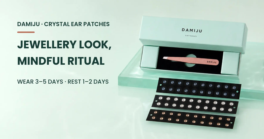 Open mint DAMIJU ear patch box with rose-gold tweezers and three crystal patch trays in blue, clear and peach