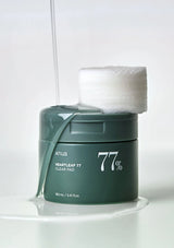Green jar of '77%' skincare product with cotton pads on a white background