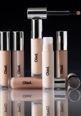 Collection of Oiad makeup products including concealers and a brush on a reflective surface with a black background.