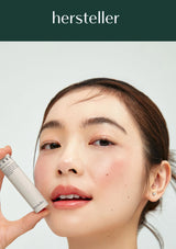 Person holding a skincare product with 'hersteller' branding on a plain background