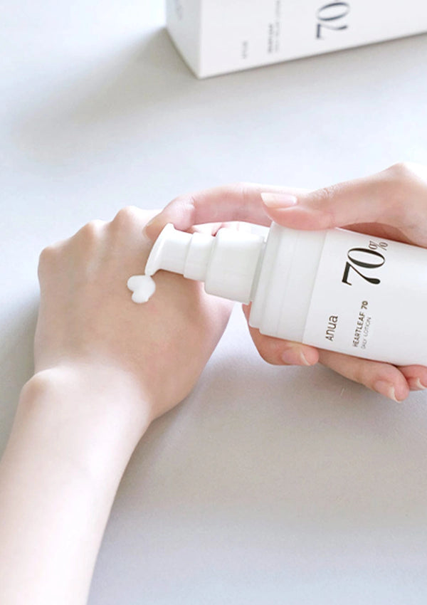 Person holding a white bottle labeled '70' with a pump, on a light surface.