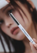 White lip pencil with black cap held by a person against a blurred background