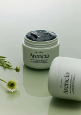 Two jars of Arencia serum on a reflective surface with flowers.