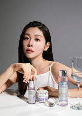 Woman sitting with skincare products on a gray background