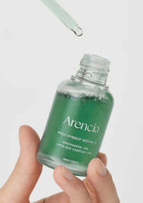 Green skincare serum bottle labeled 'Arencia' held by a hand with a dropper above it on a light gray background.